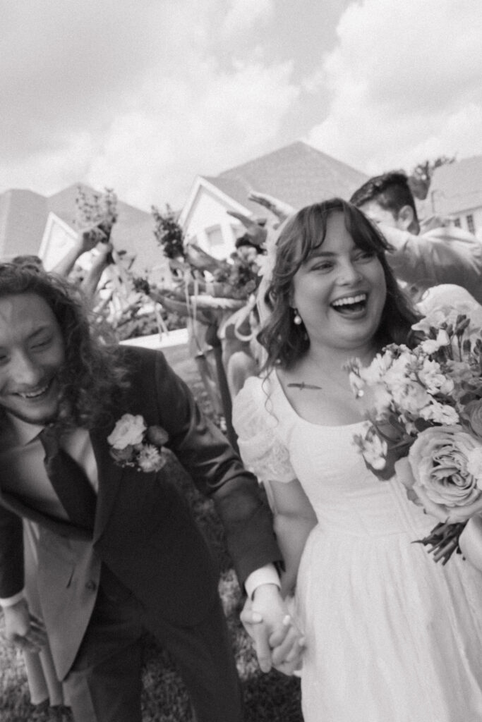 Bride and groom laughing as they run through cheering guests after ceremony.