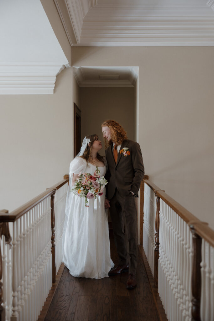 Bride in vintage-inspired dress and groom in brown suit with orange tie — editorial couple portrait.